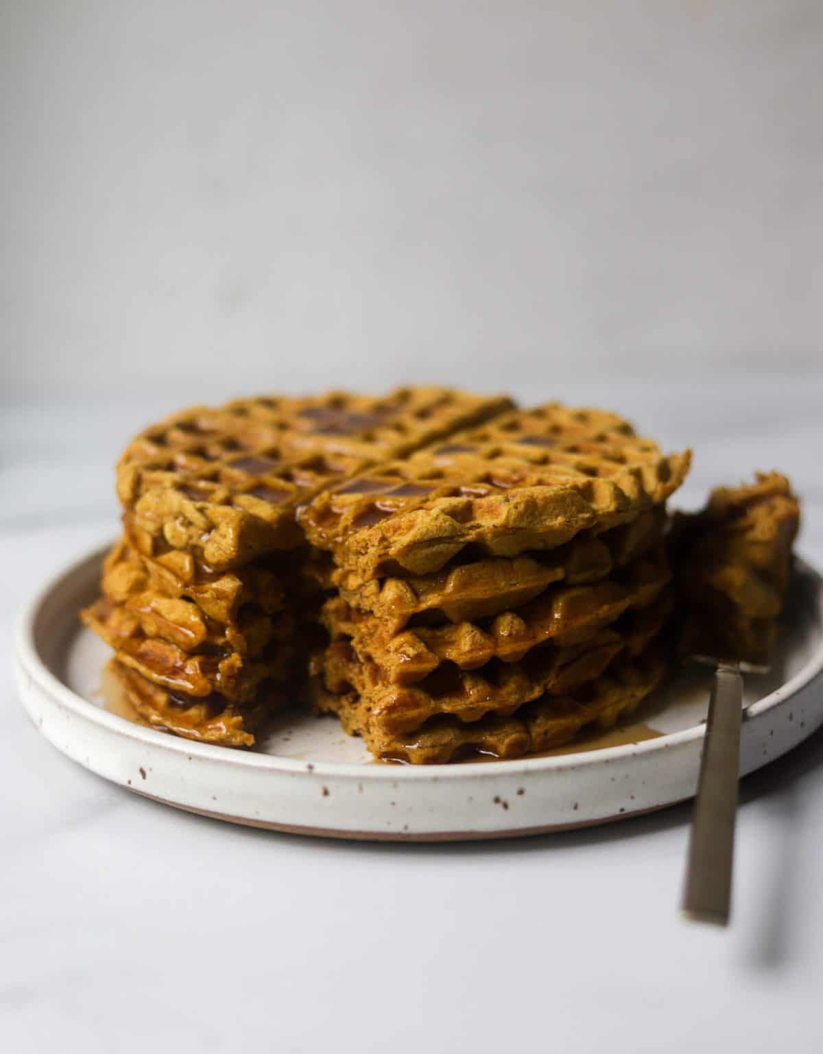 A straight on shot of a plate of stacked pumpkin waffles with syrup dripping.
