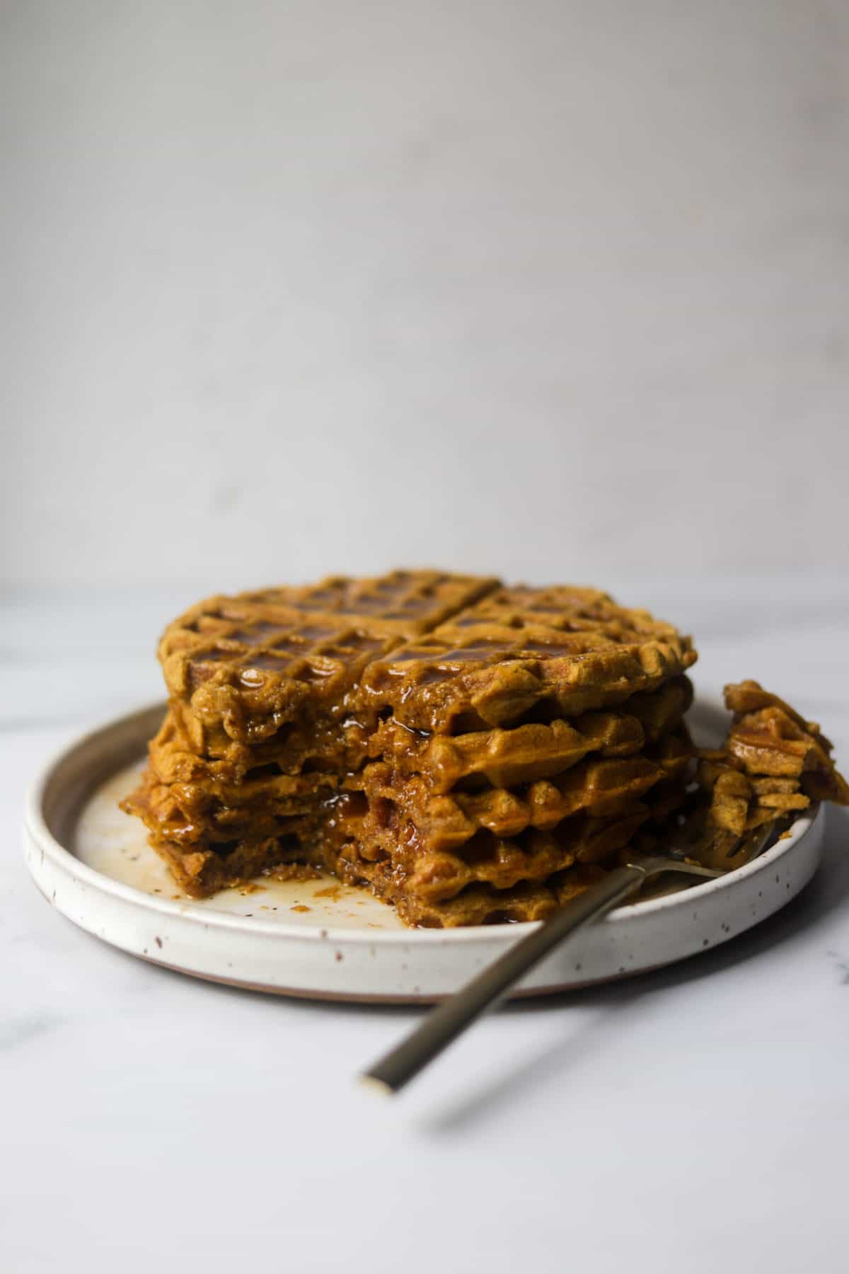 A straight on shot of a stack of pumpkin waffles and syrup dripping with a fork.