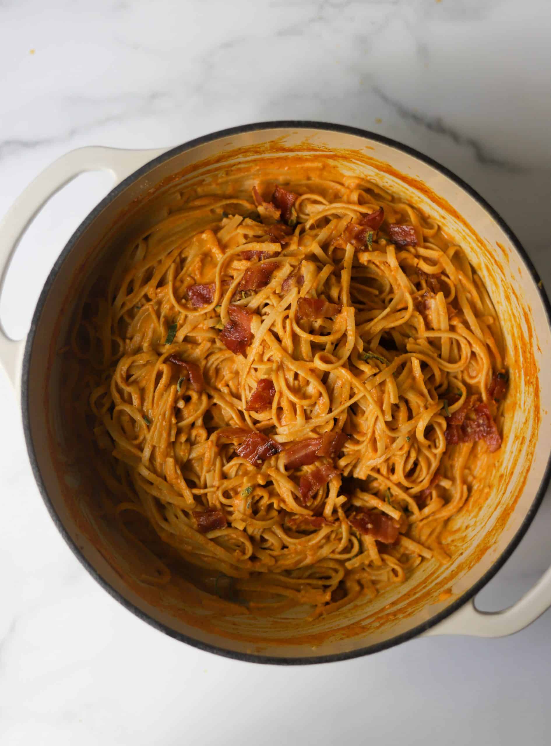 A white Dutch oven filled with pumpkin pasta with bacon.