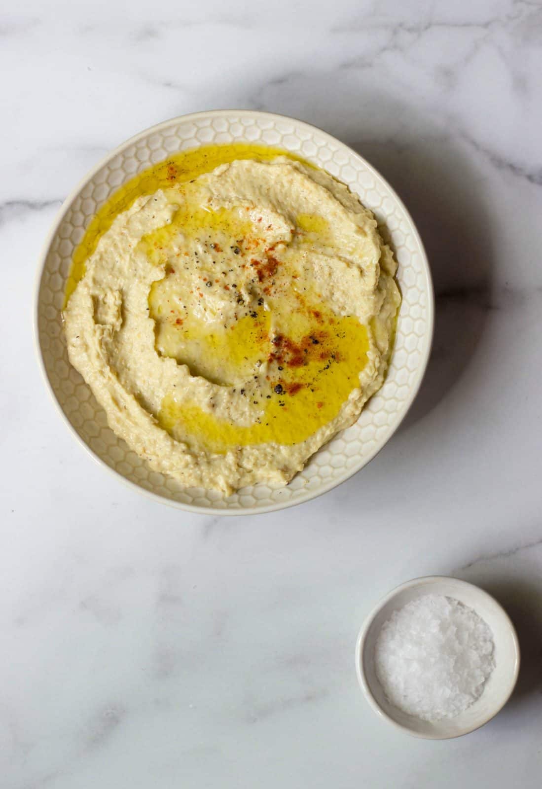 Overhead shot of hummus in a white dip bowl and a side of salt in a small white dish. 