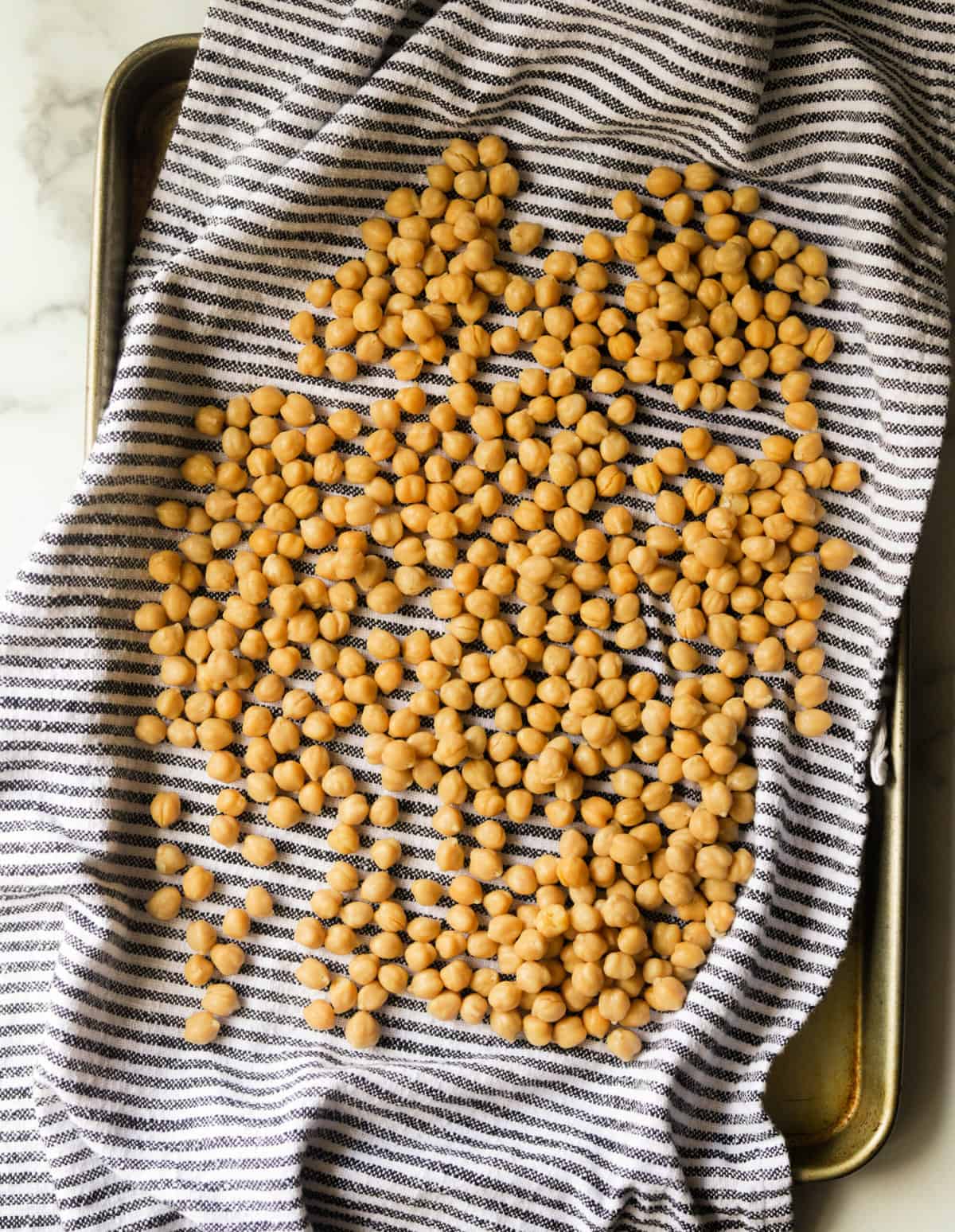 An overhead shot of a pan of chickpeas being dried with a kitchen towel.