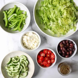 Greek salad ingredients in white bowls
