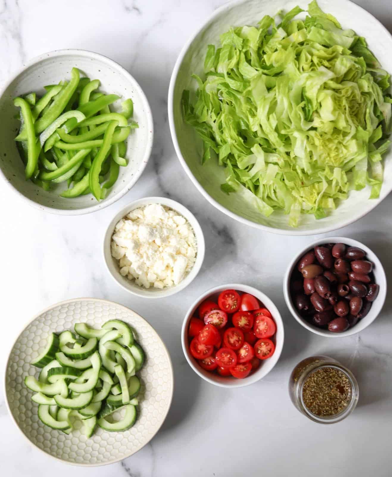 Greek salad ingredients in white bowls