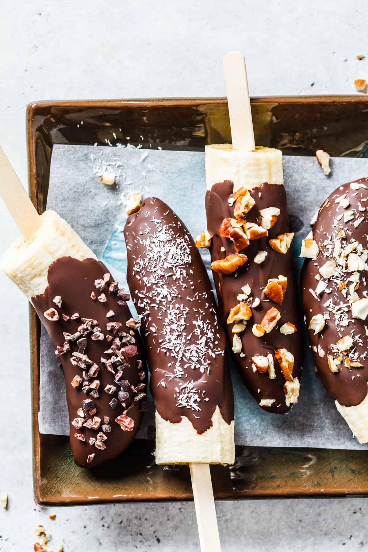 An overhead shot of frozen banana chocolate pops on a popsicle stick.