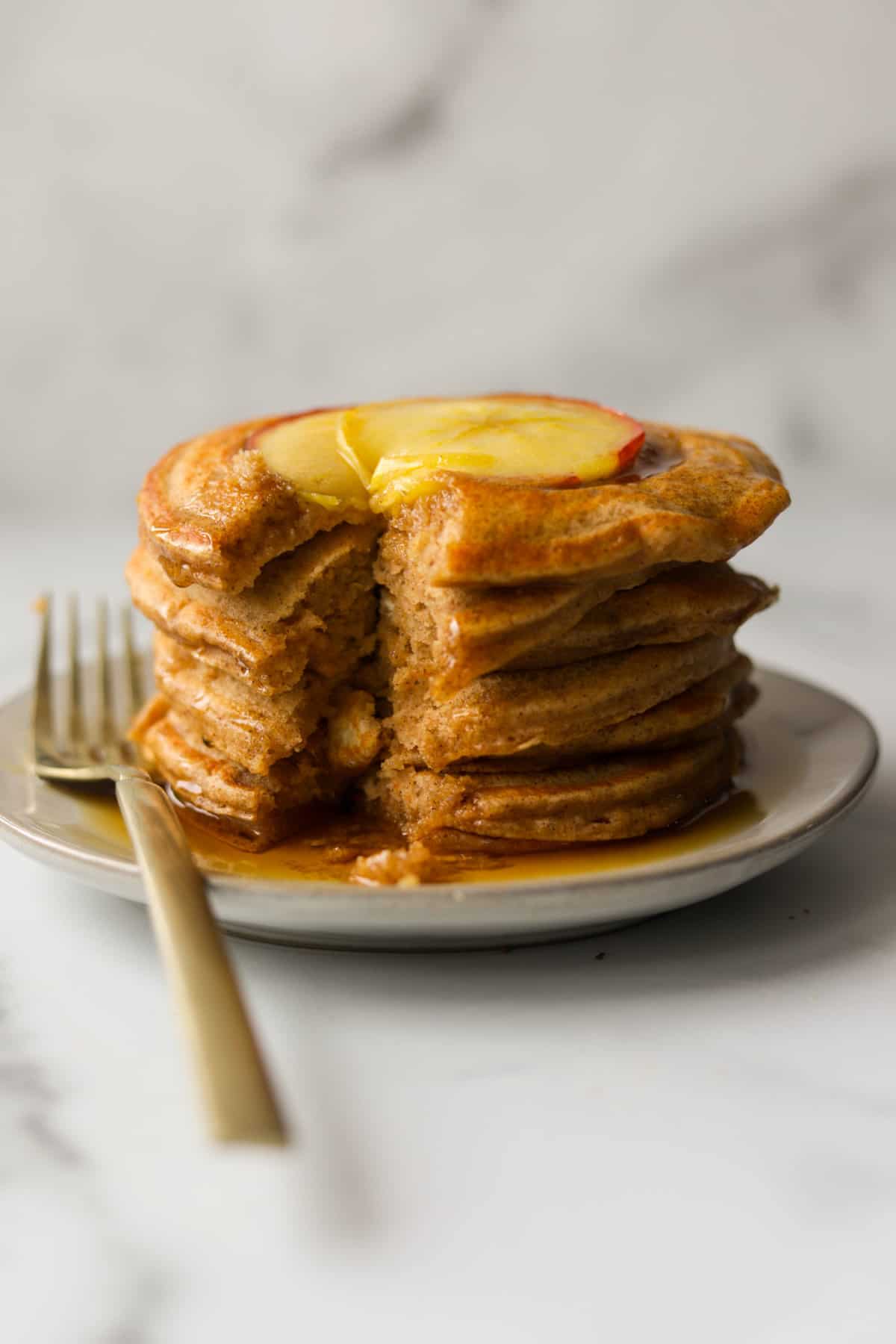 A side shot of a stack of apple cinnamon pancakes with a bite missing.