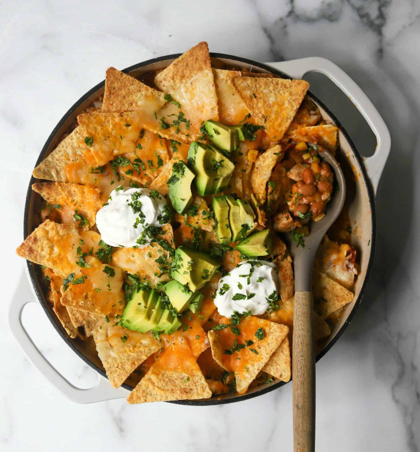 Chicken taco casserole in a white dutch oven with a serving spoon scooping some out.