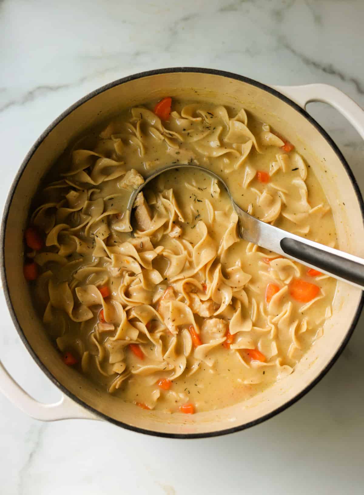 An overhead shot of a pot of creamy chicken noodle soup.