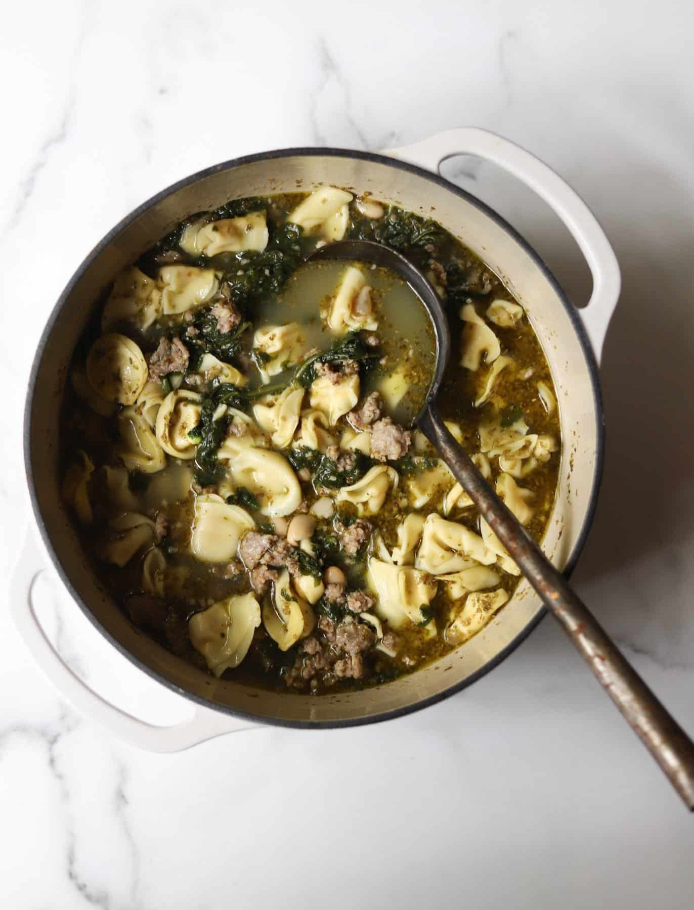 Tortellini soup in a white pot made with cannellini beans. 