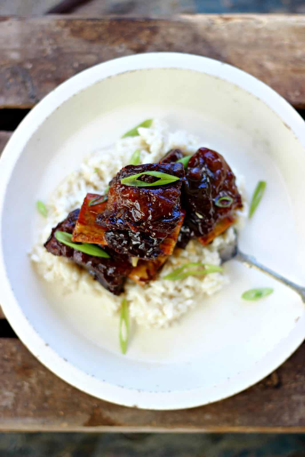 Overhead shot of ginger beef short ribs on top of rice in a white bowl. 