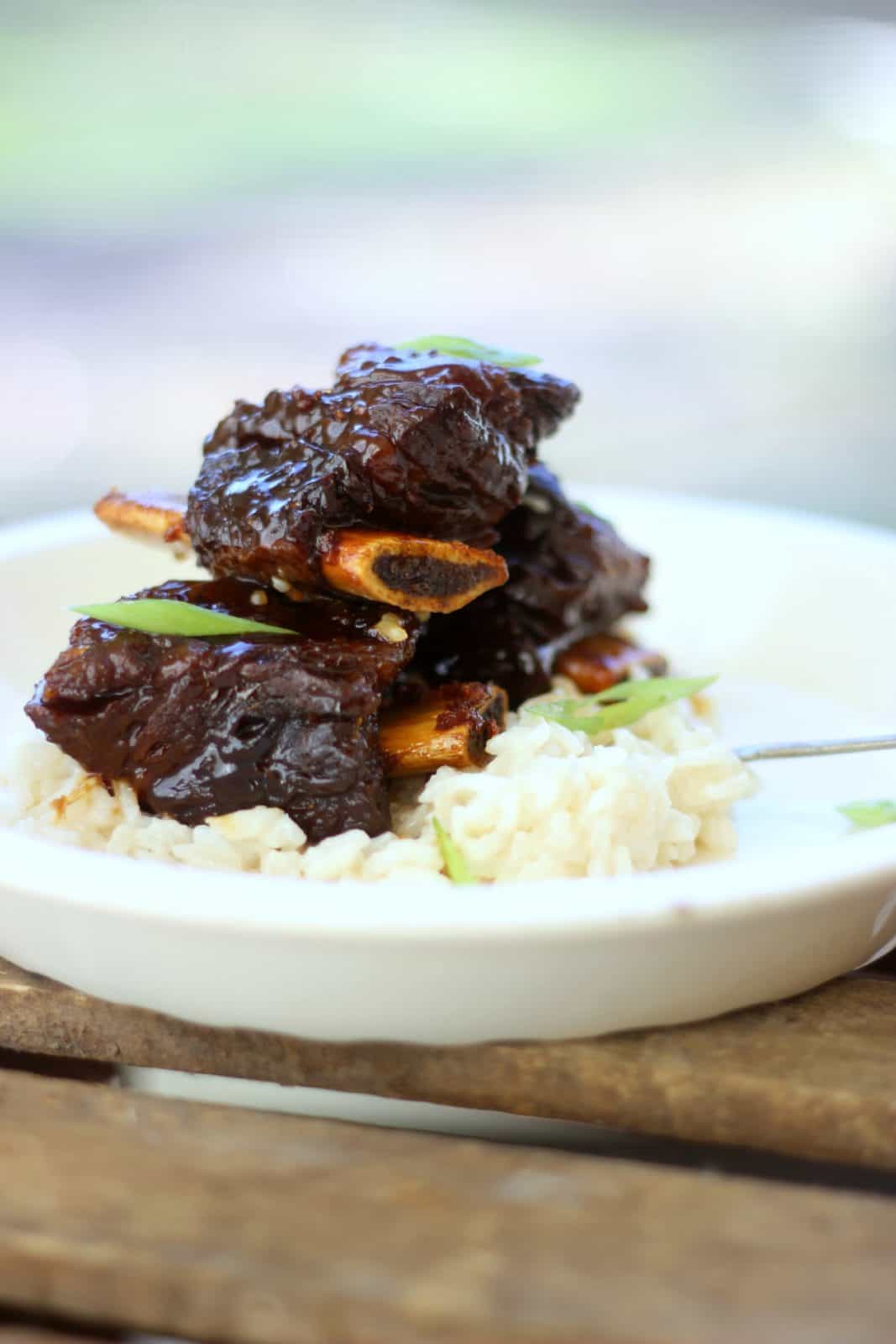 Side shot of ginger beef short ribs on top of rice in a white bowl. 