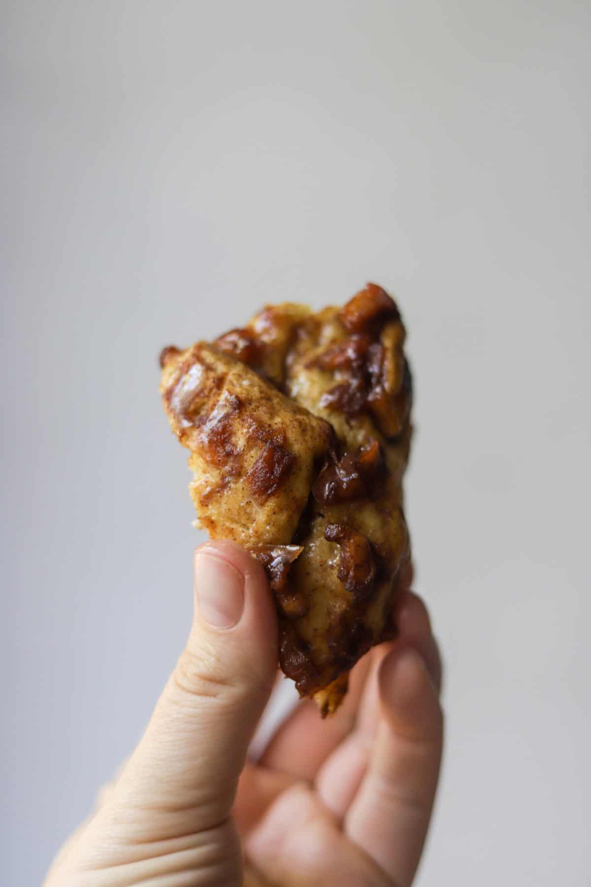A hand holding a chunk of apple fritter bread.