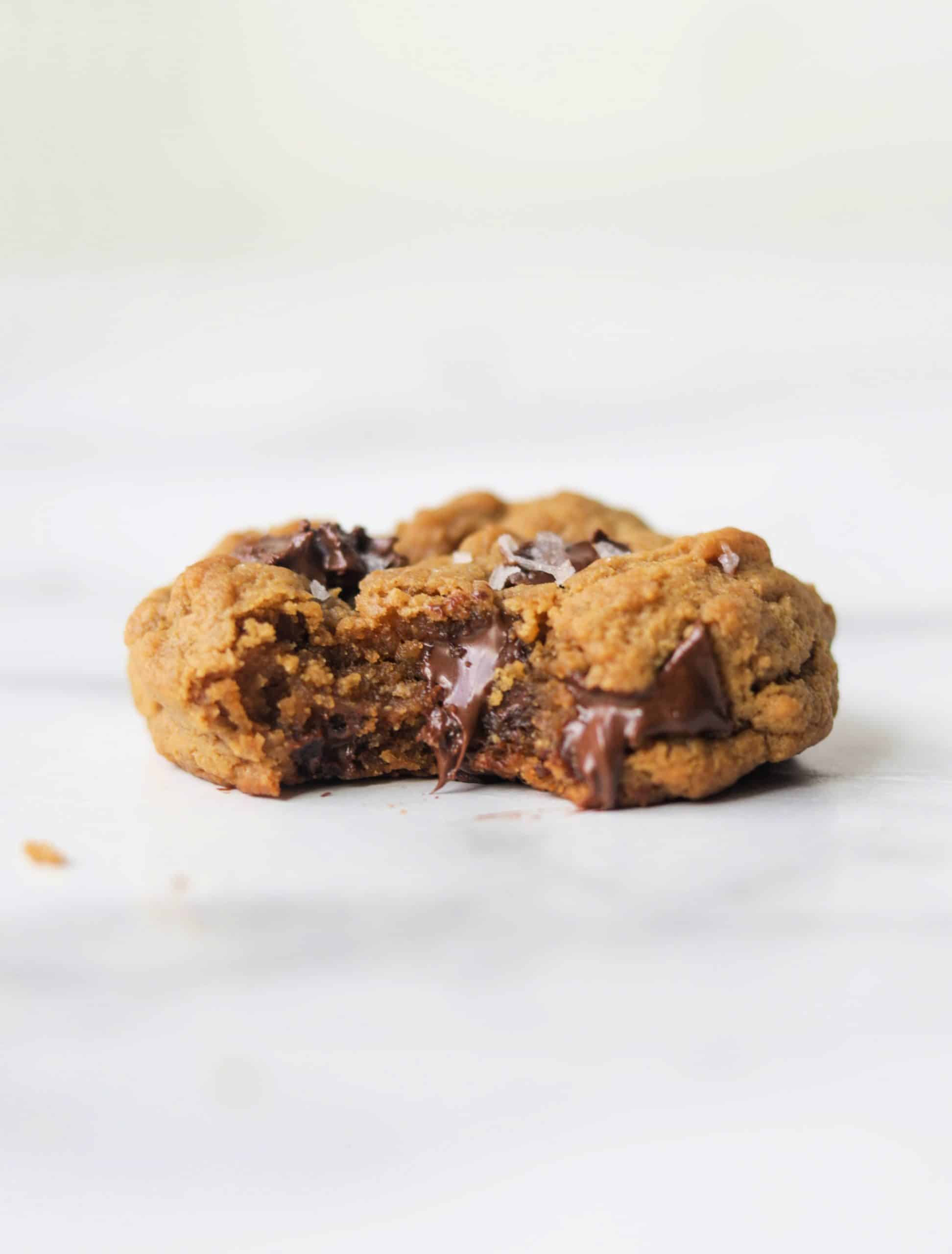 A single peanut butter cookie with dark chocolate on a white marble backdrop.