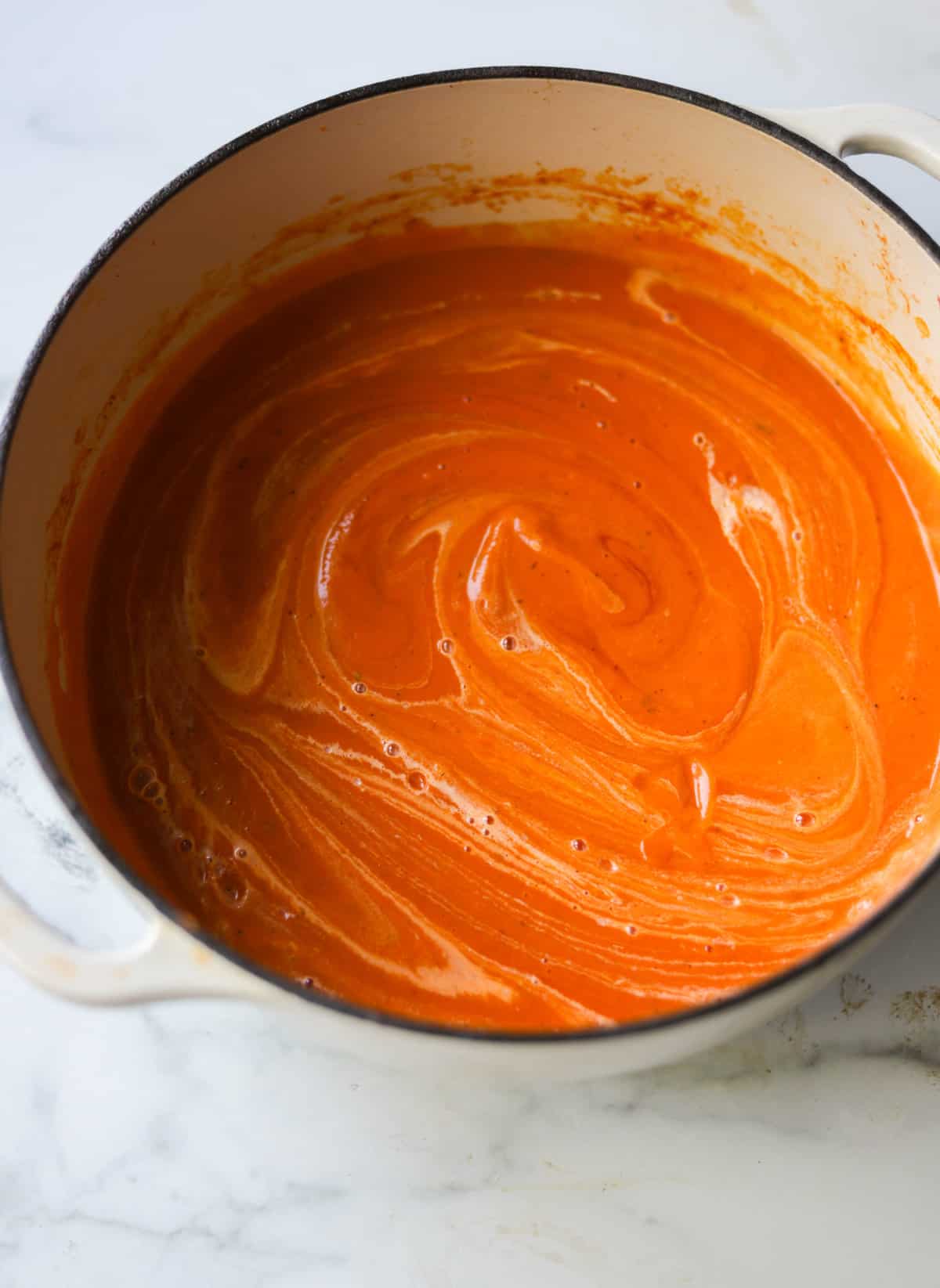 A side shot of a pot of creamy tomato soup with cream swirled into it.