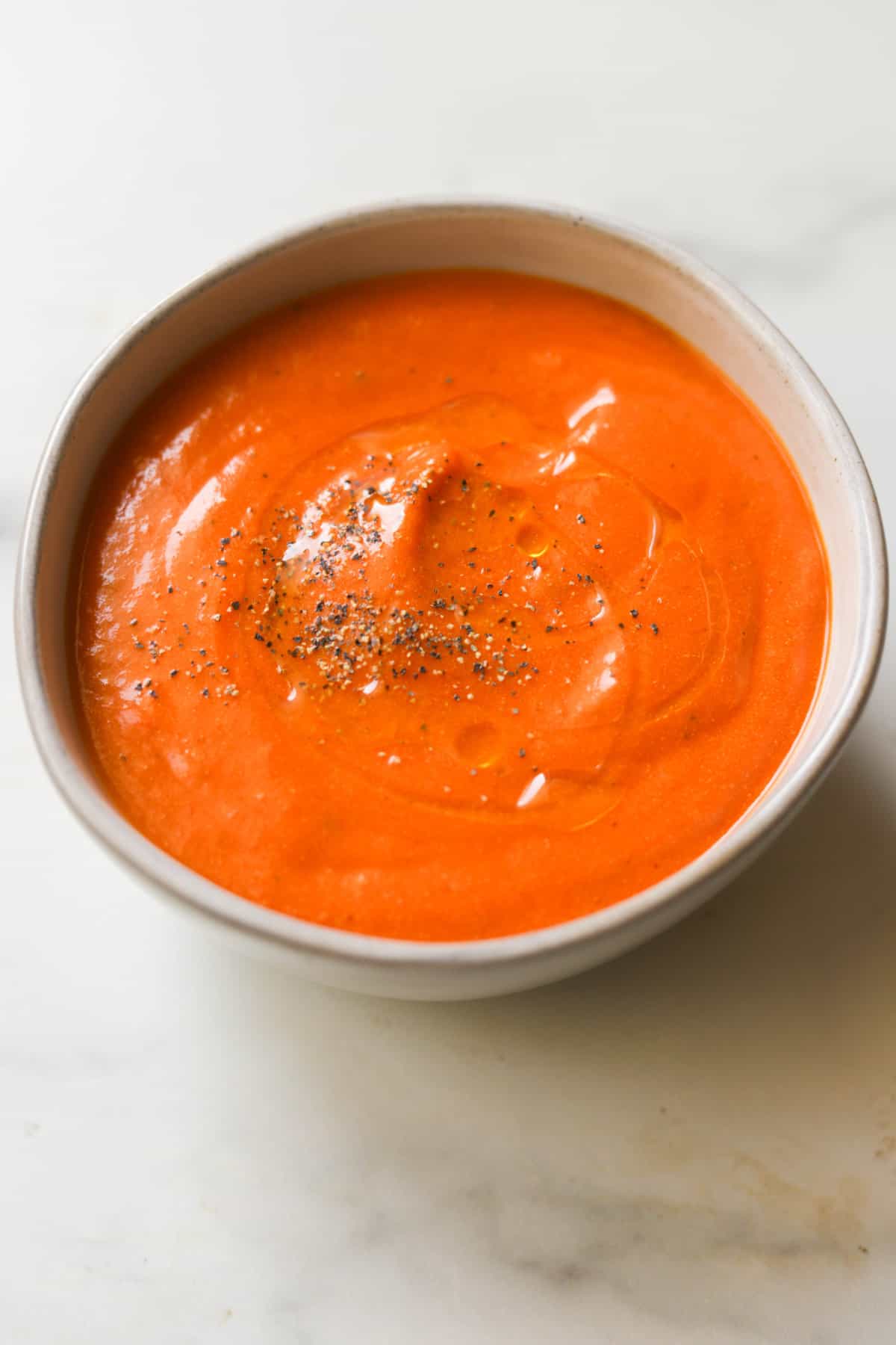 A side angled shot of a bowl of creamy tomato soup with black pepper sprinkled on top.