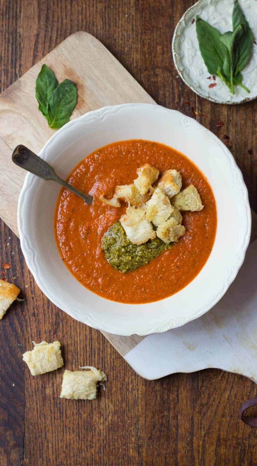 Overhead shot of tomato soup with pesto and garlic bread croutons in a white bowl. 