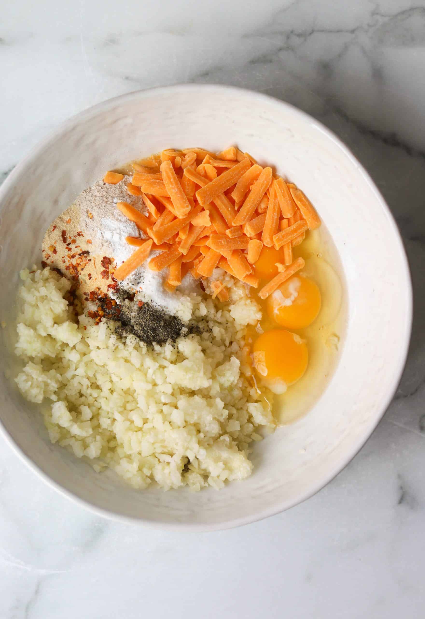 A white bowl with eggs, riced cauliflower, flour, shredded cheese and spices.