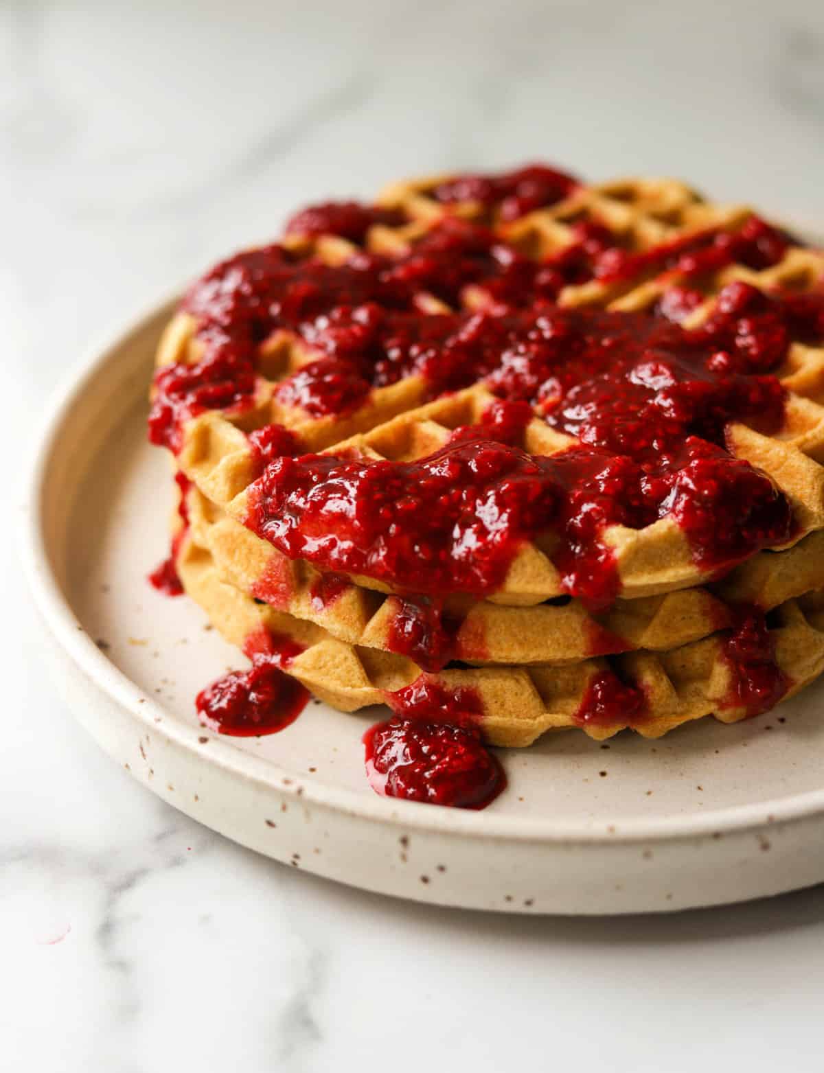 A side shot of a stack of lemon waffles drizzled with berry syrup.