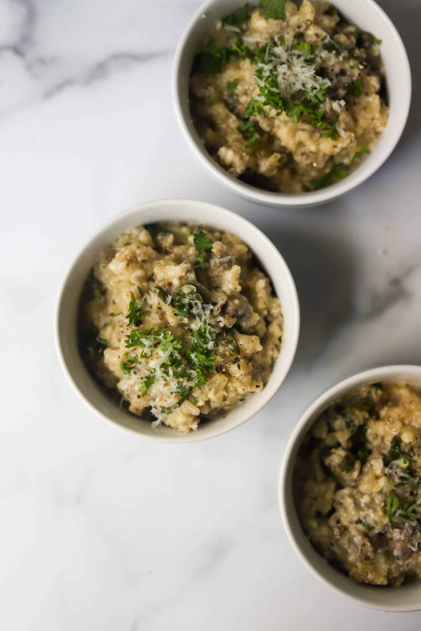 Three bowls of risotto on a marble backdrop.