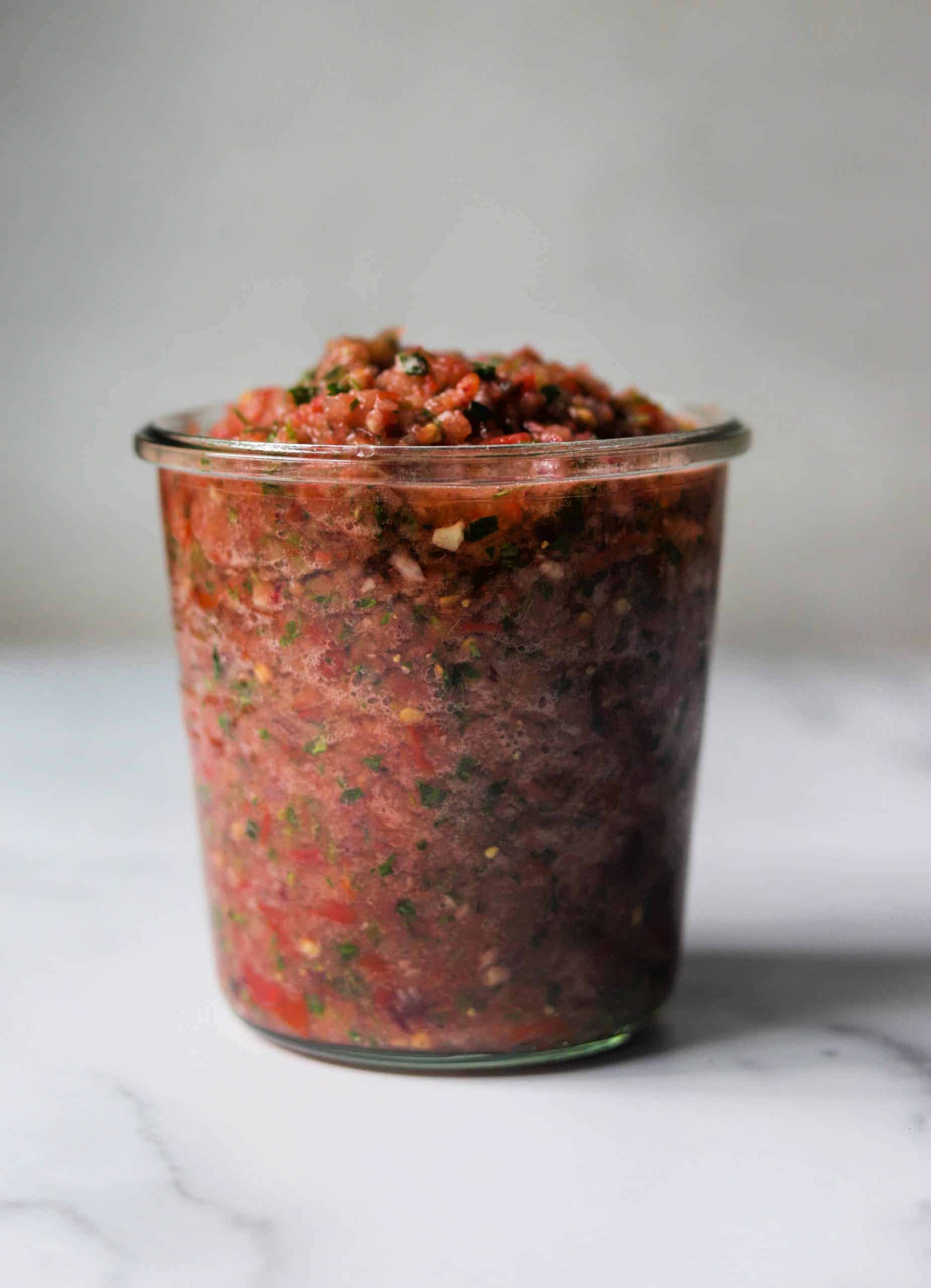 A clear jar filled with tomato jalapeno salsa.