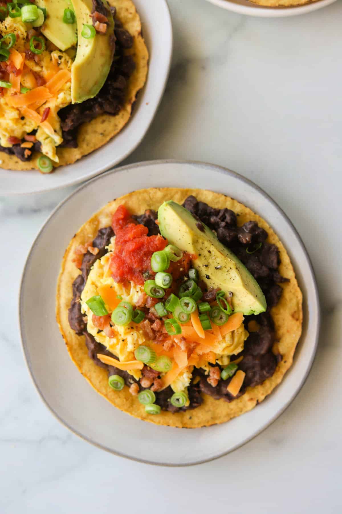 An overhead shot of a few plates of breakfast tostadas with avocado and salsa on top.