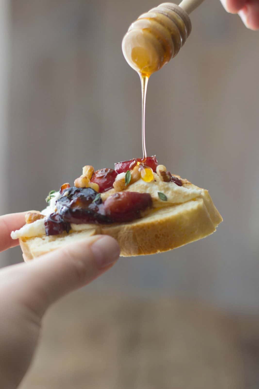 Roasted balsamic grapes & creamy lemon ricotta dip on a baguette slice with honey being drizzled on top.