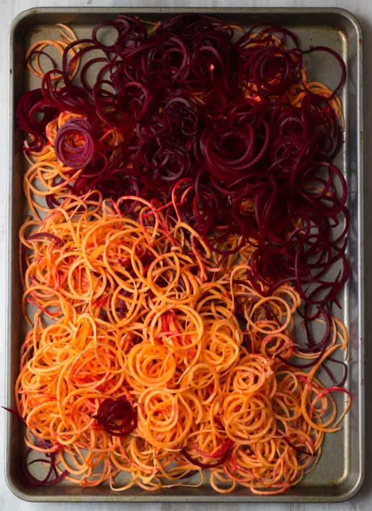Sweet potato and beet curly fries on a baking sheet.