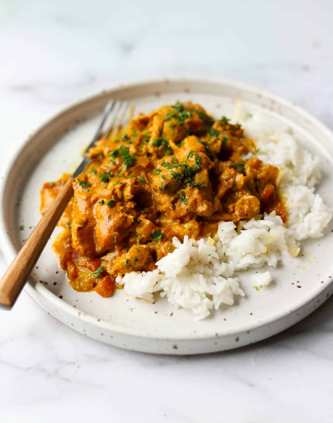 A side shot of a plate of butter chicken and white rice.