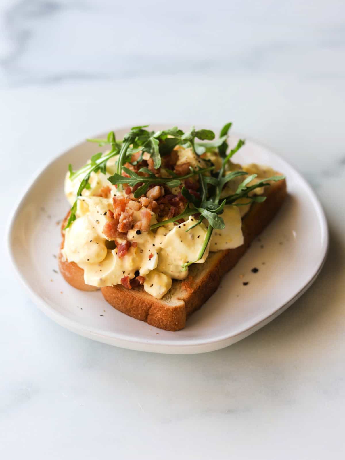 A side angled shot of an open faced egg salad sandwich.