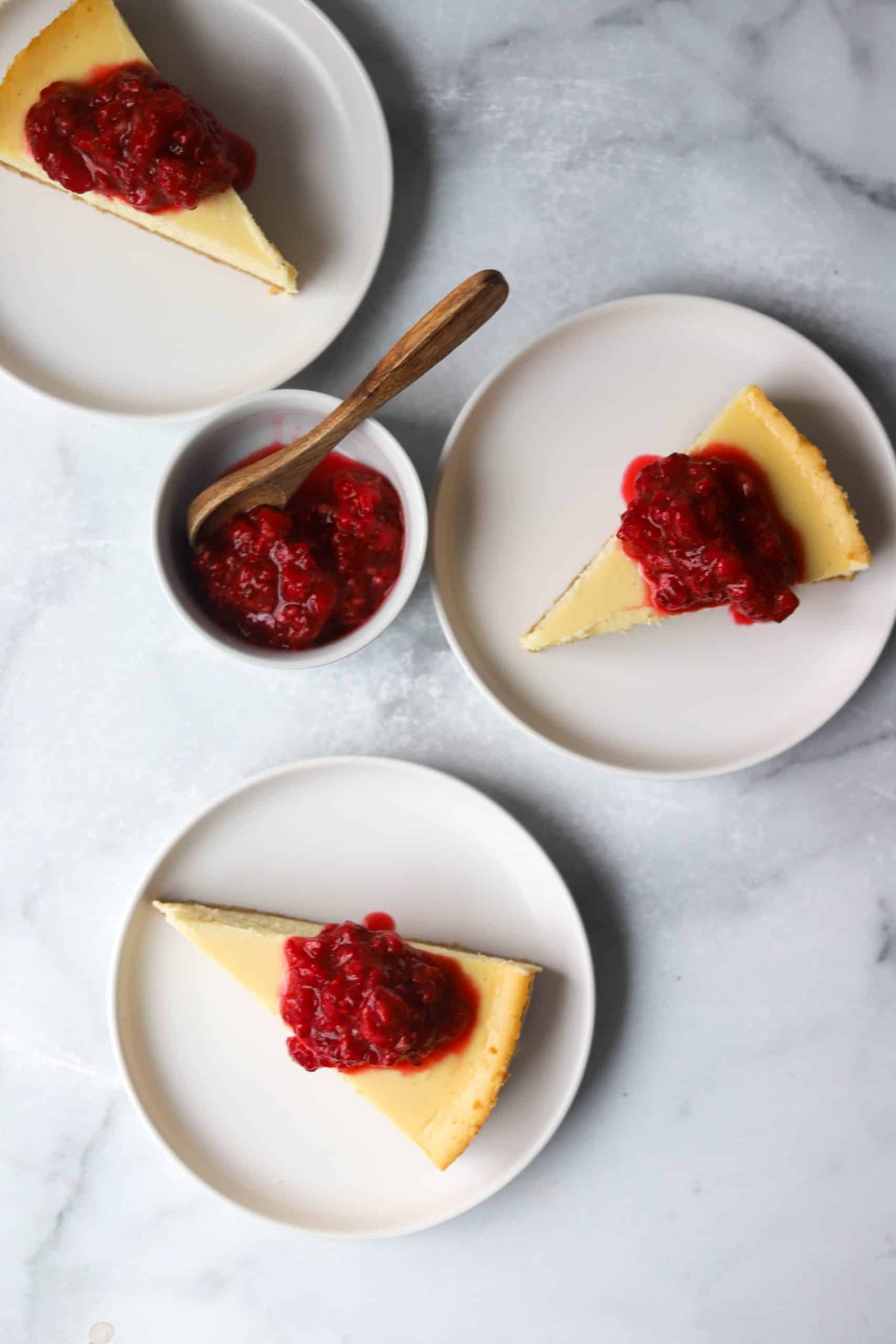 Three plates with slices of cheesecake and a small bowl of raspberry topping.