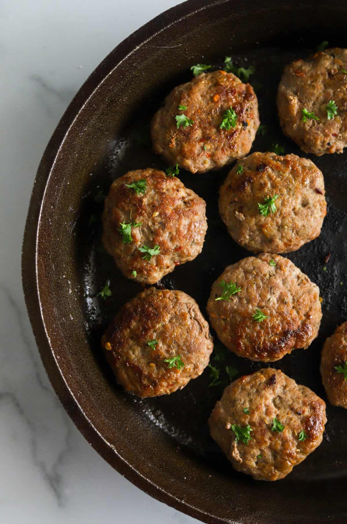 An overhead shot of a cast iron skillet with breakfast sausage patties.