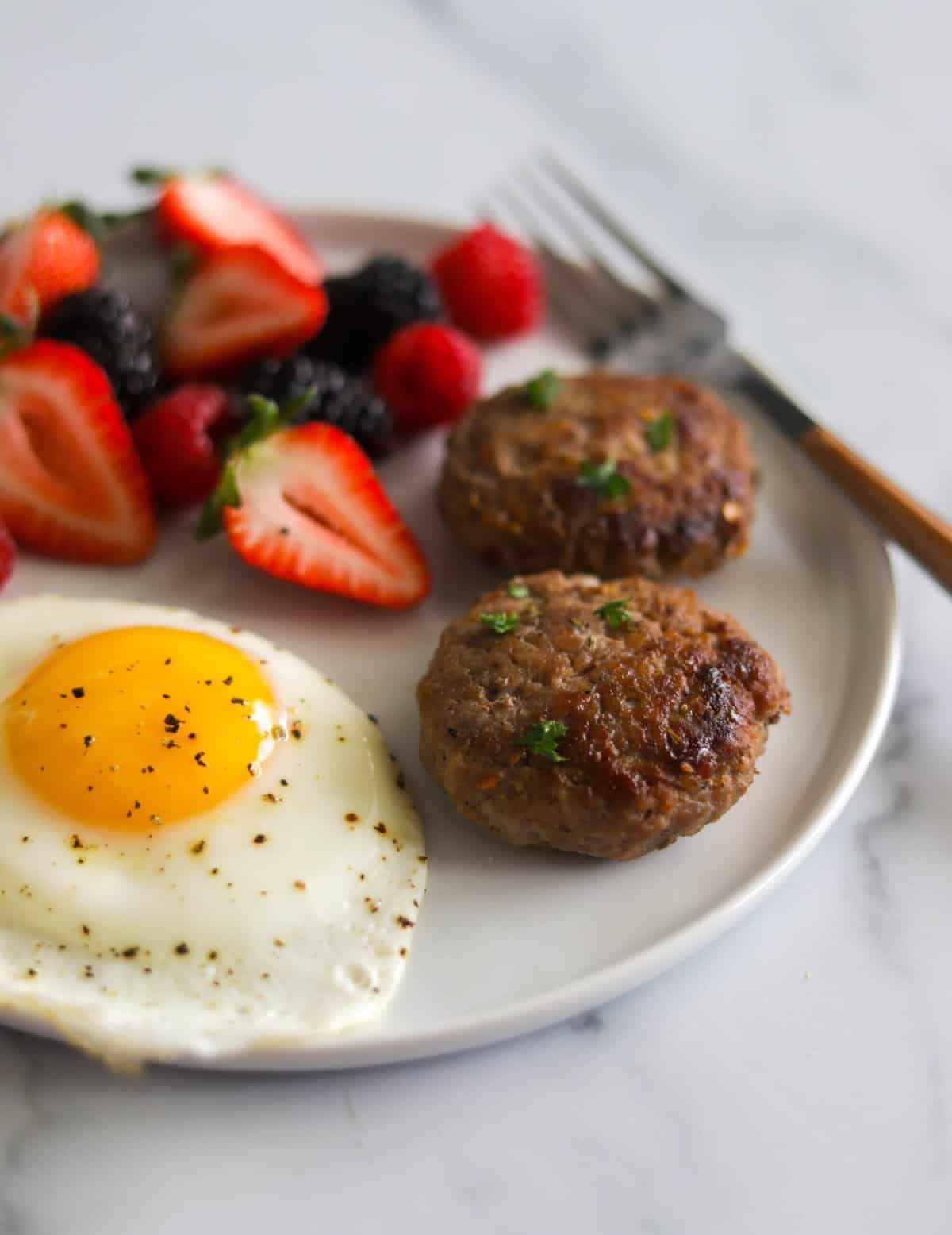 A side shot of a plate of breakfast sausage, a fried egg and berries.