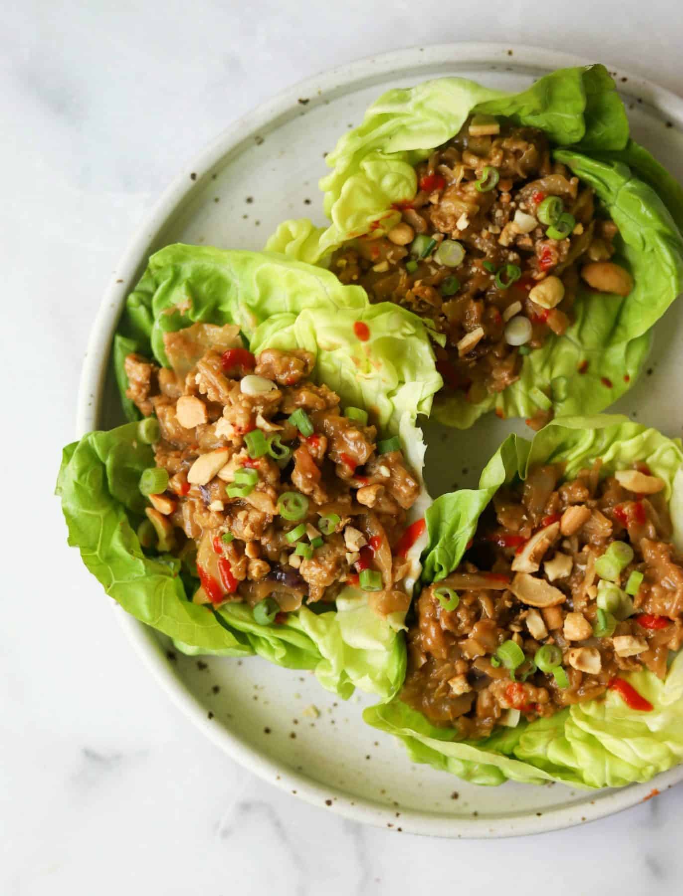 Cashew chicken lettuce wraps on a white speckled plate as an example for ways to eat more leafy greens. 