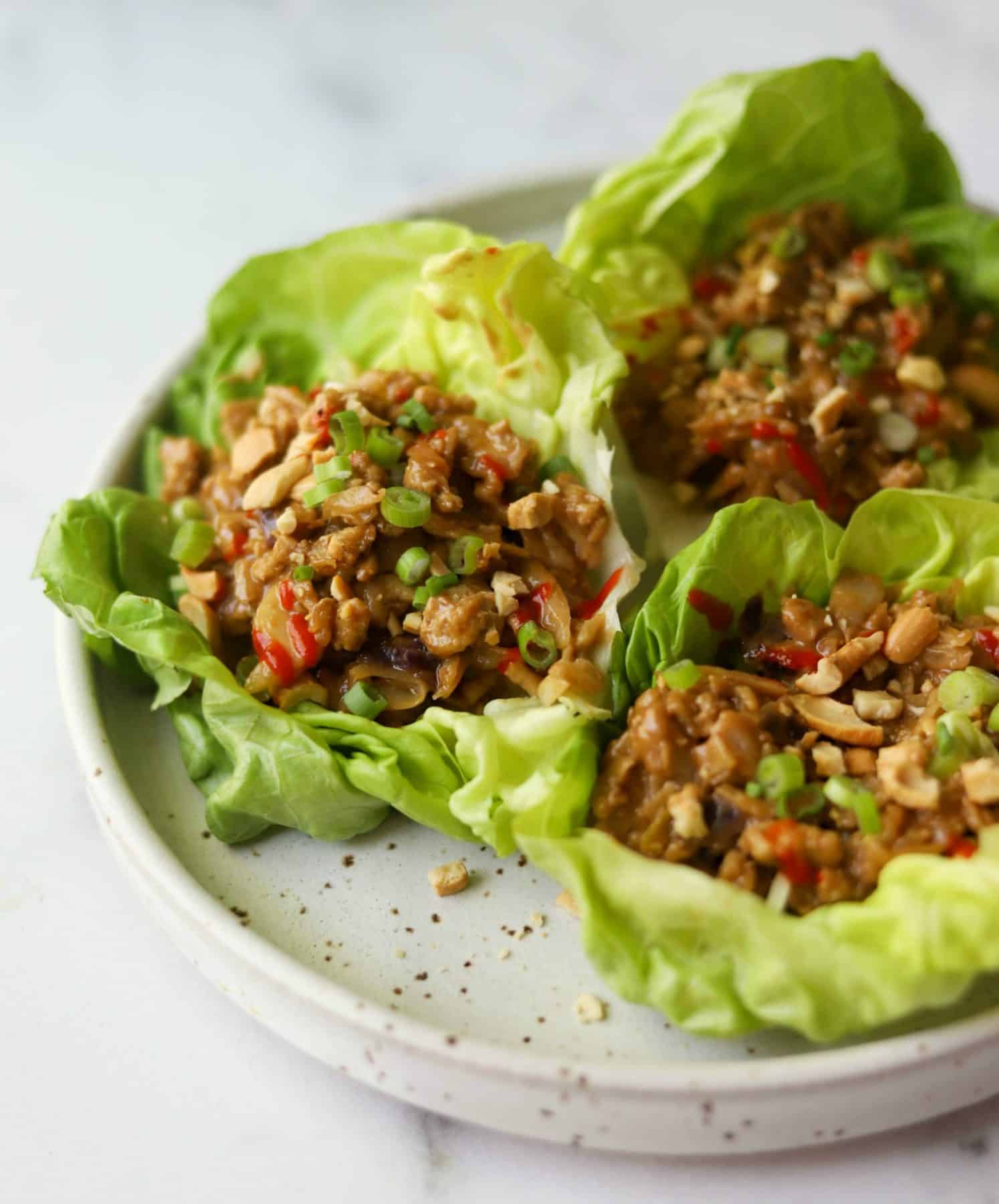 Cashew chicken lettuce wraps on a white speckled plate