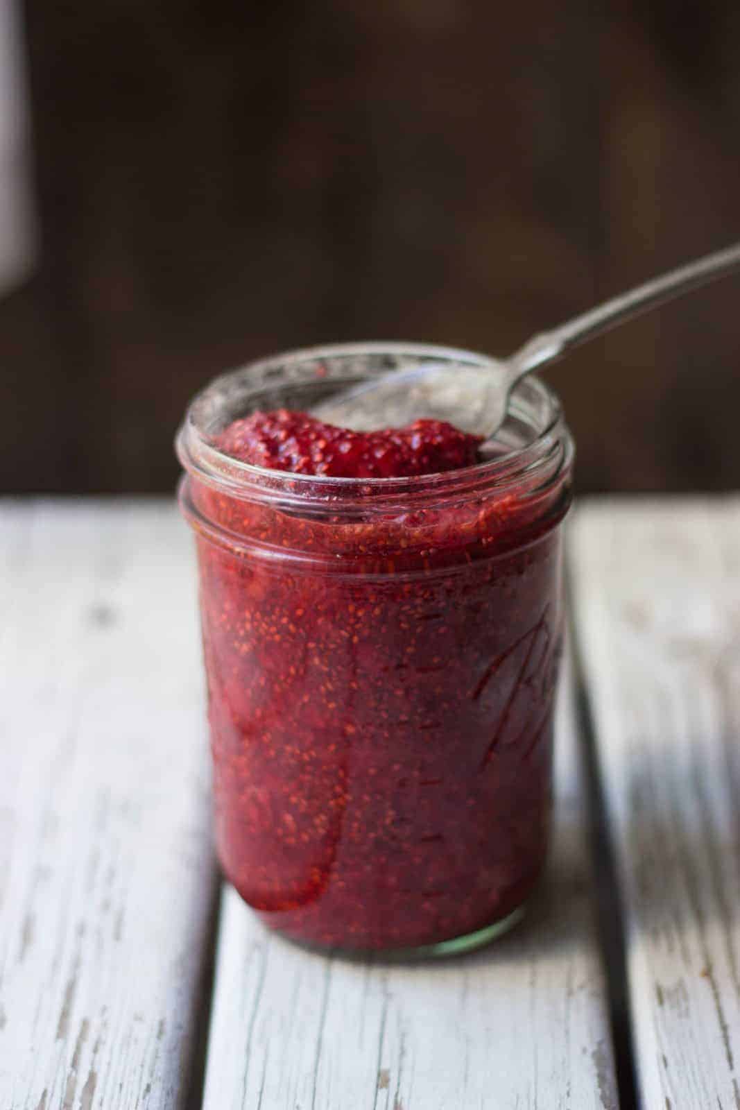 Strawberry jam in a clear jar with a silver spoon in it.