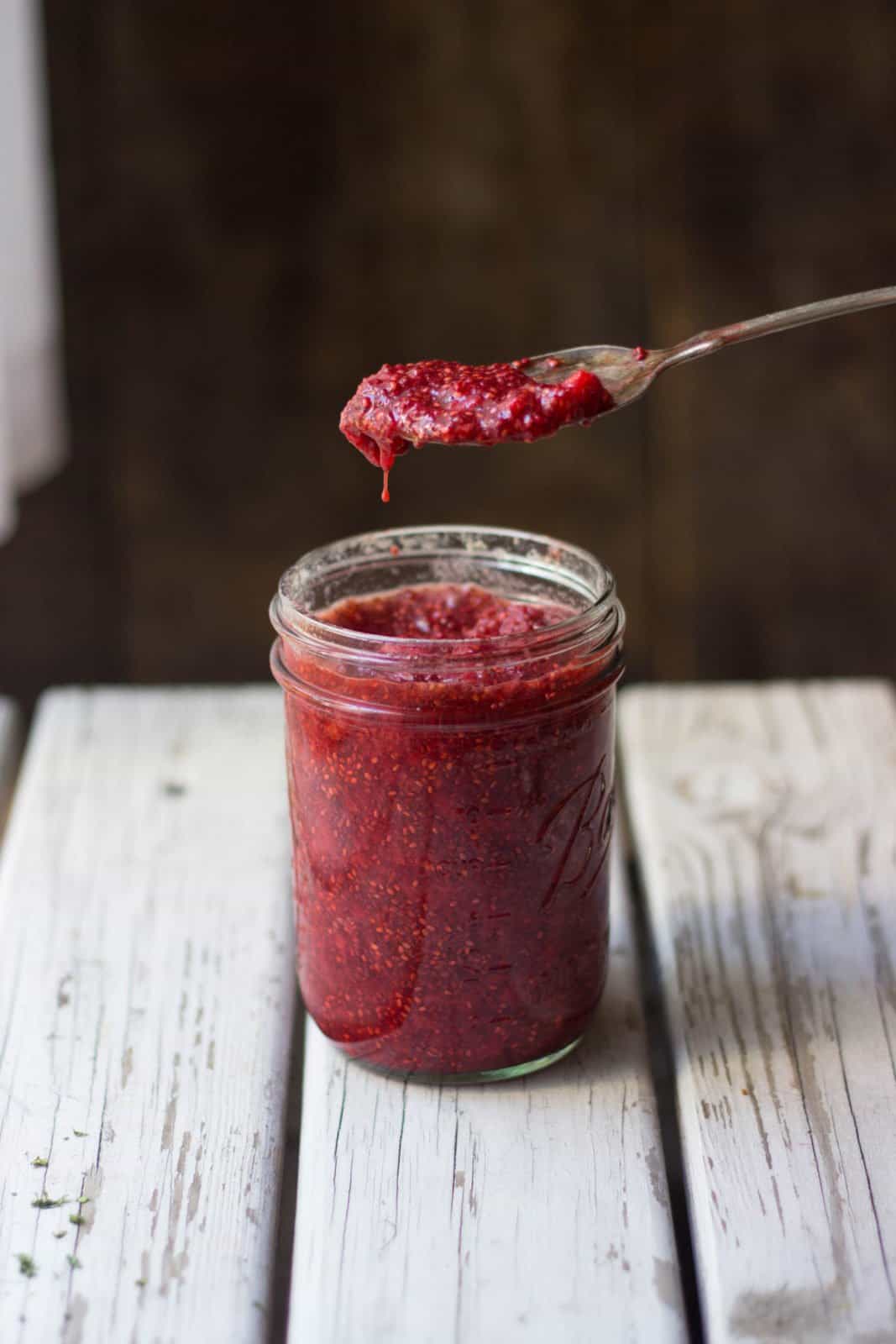 Strawberry jam in a clear jar with spoon scooping jam out of it. 