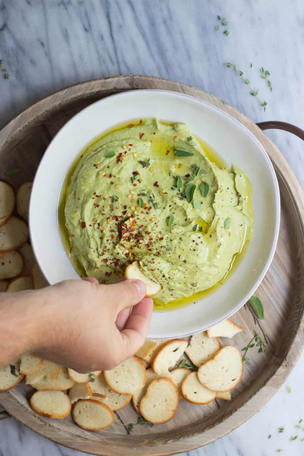 Whipped avocado white bean dip being dipped in a white bowl
