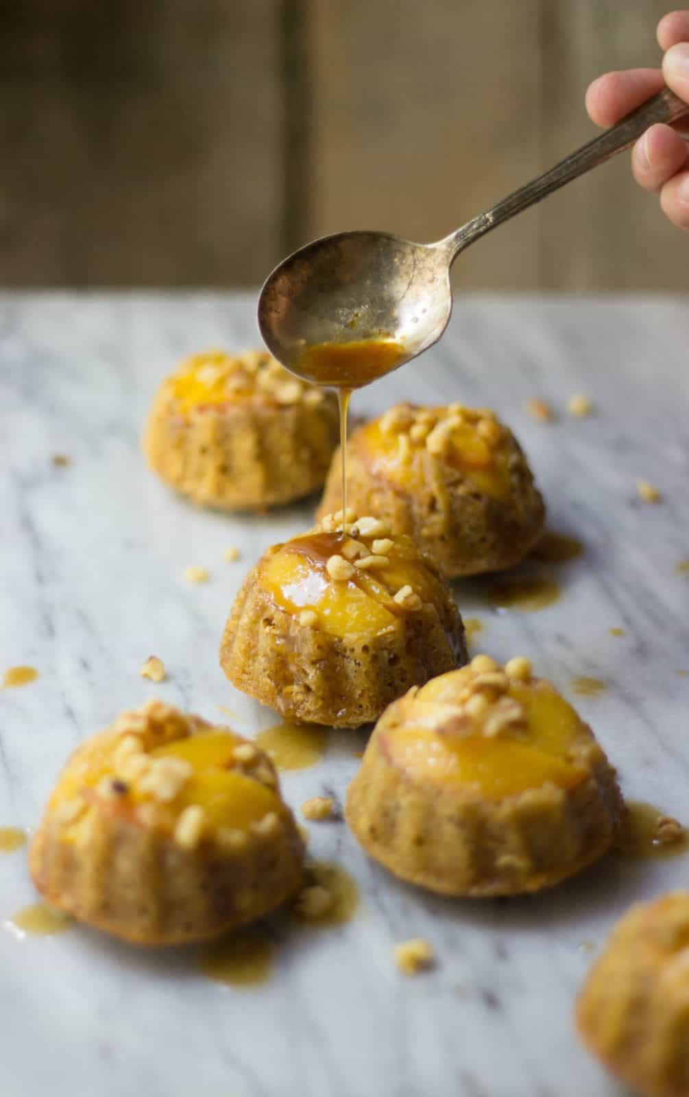 MIni peach bundt cakes on a marble board with a spoon pouring brown sugar syrup