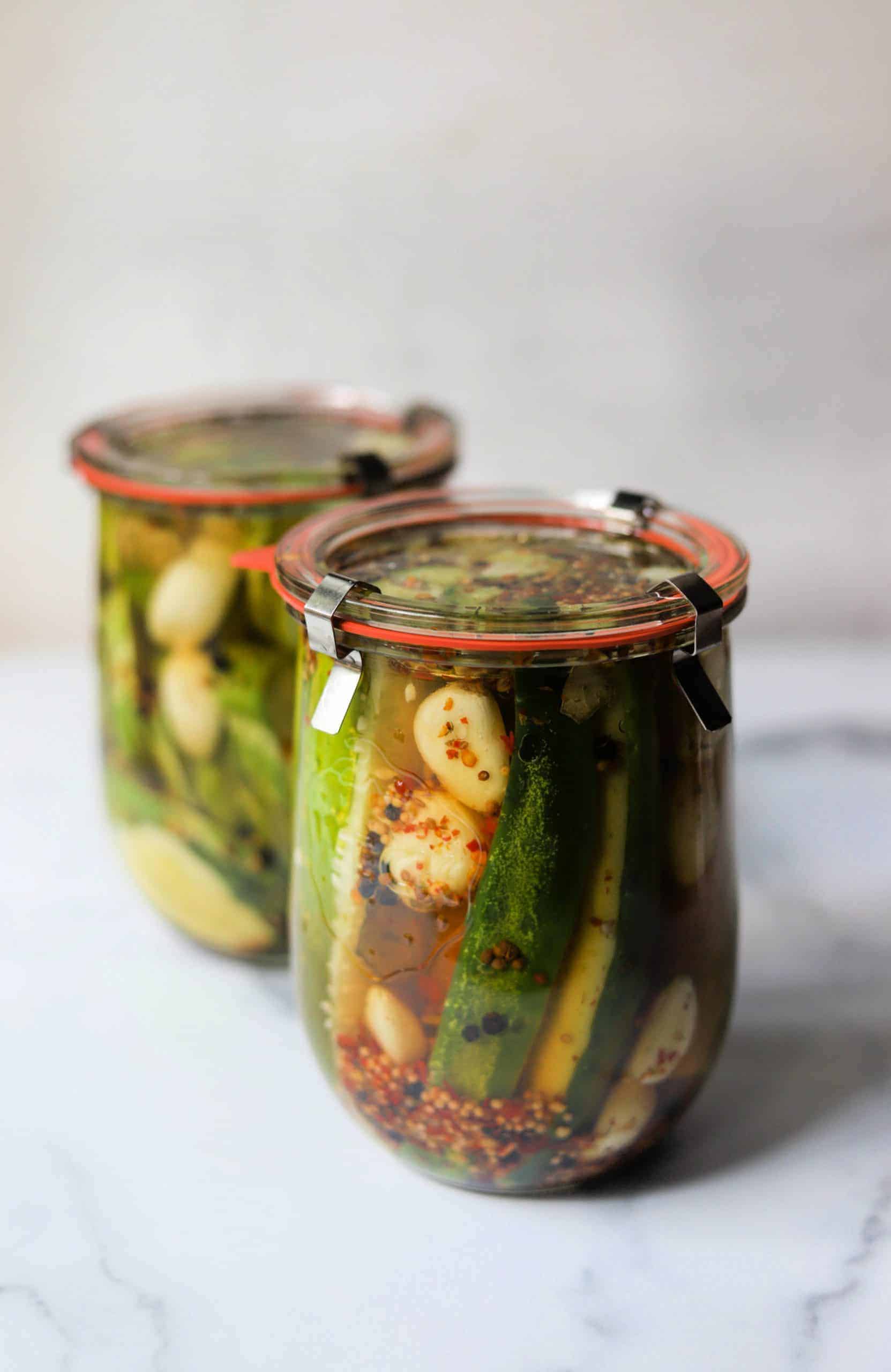 Two jars of homemade pickles on a marble backdrop.