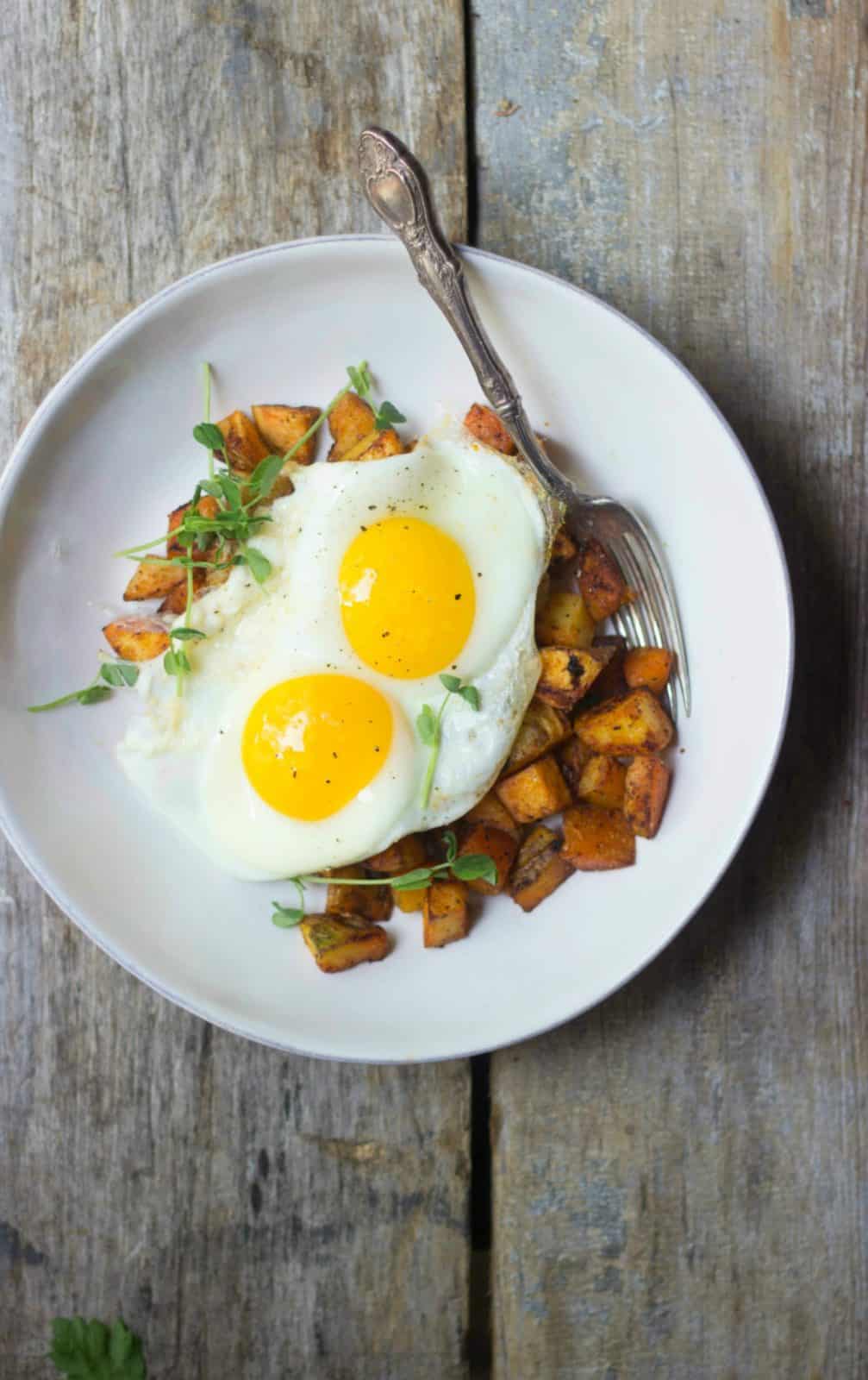 Crispy breakfast potatoes with fried eggs in a white bowl