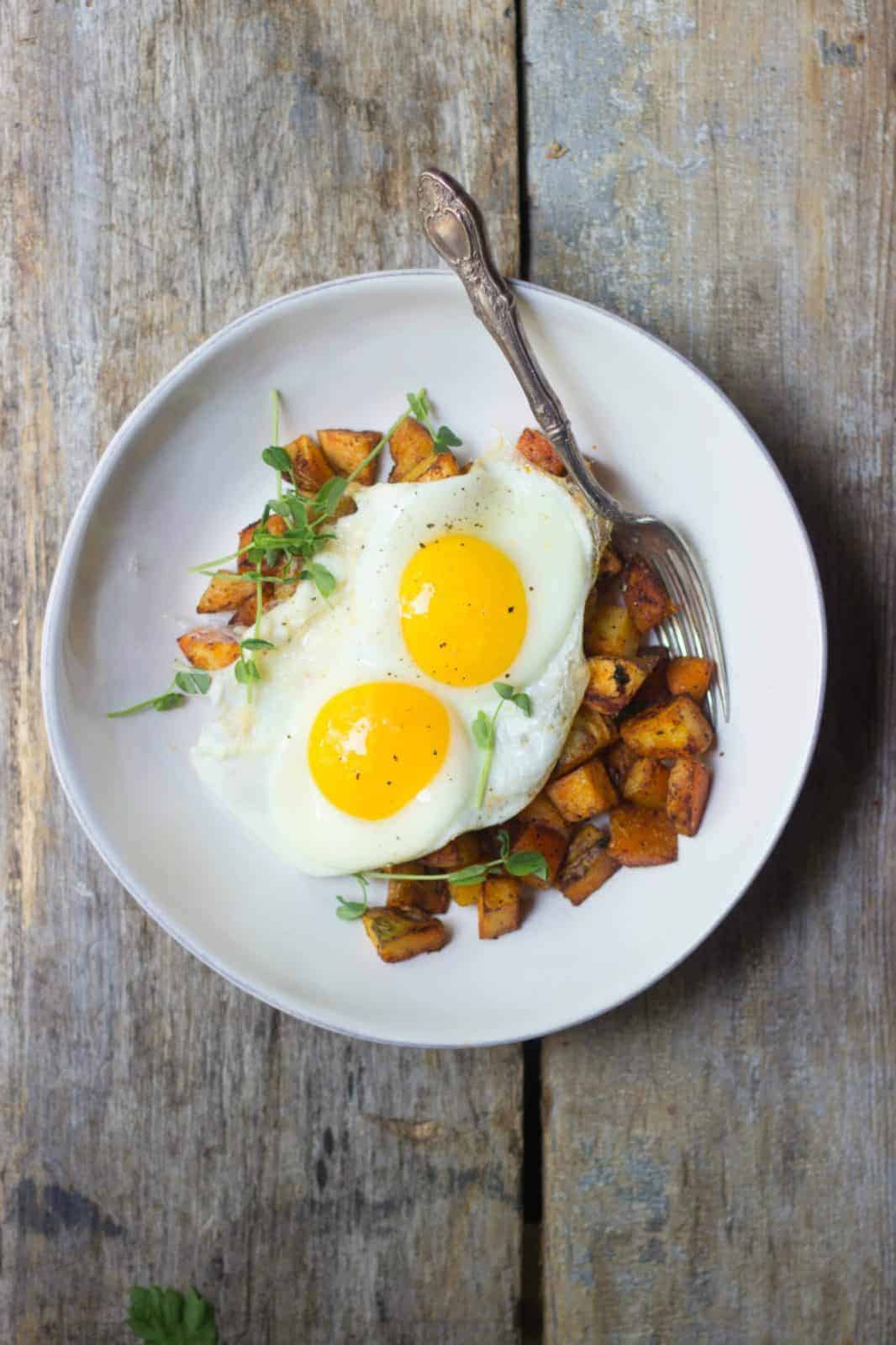 Crispy breakfast potatoes with fried eggs in a white bowl