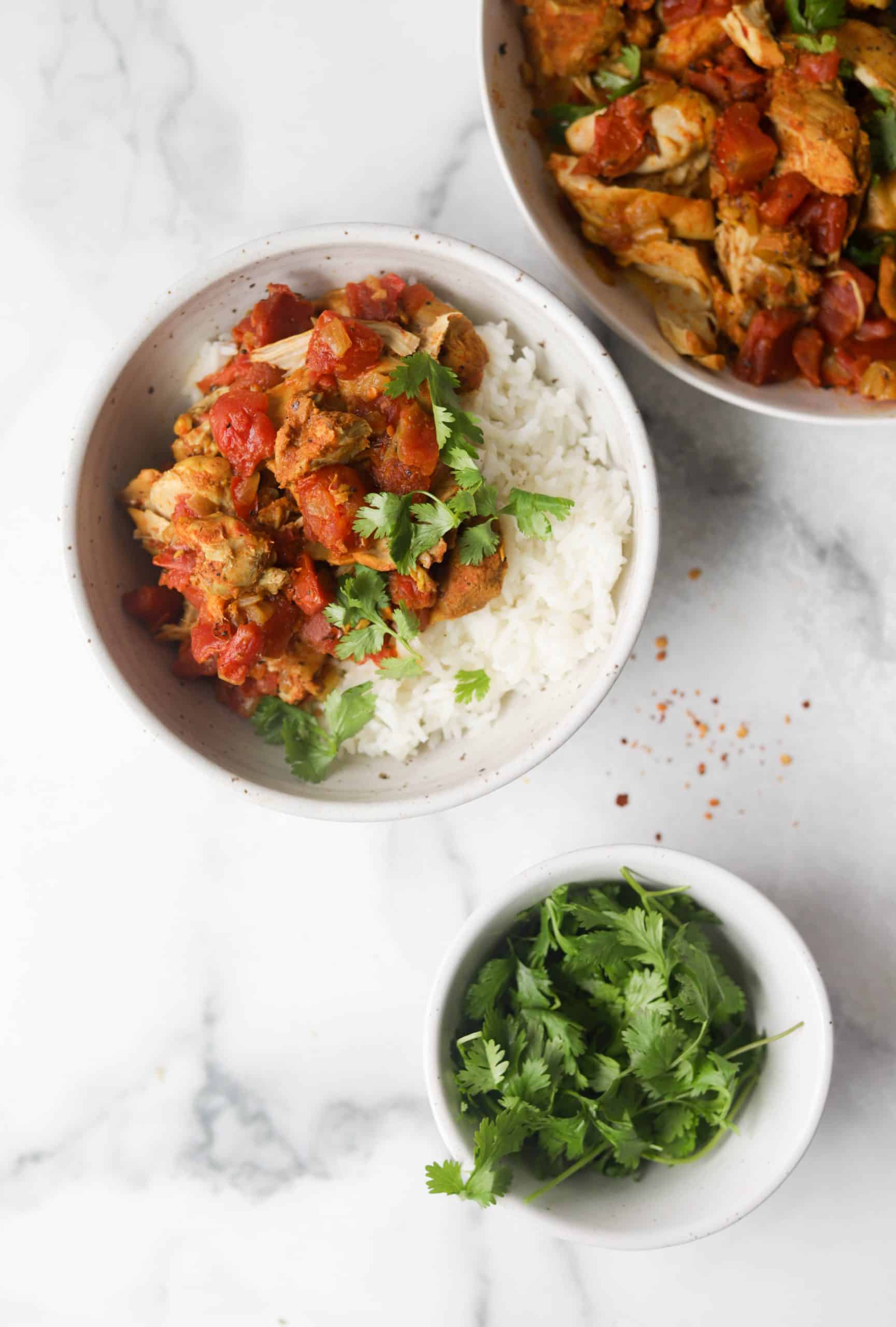 A bowl with Jasmine rice and vindaloo chicken with a side bowl of vindaloo chicken and cilantro.
