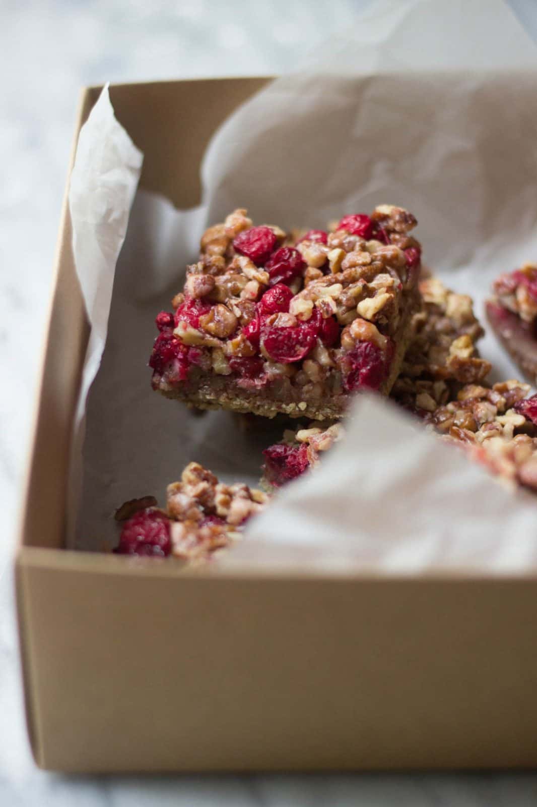 Angle shot of cranberry pecan bars in a container with white parchment paper.