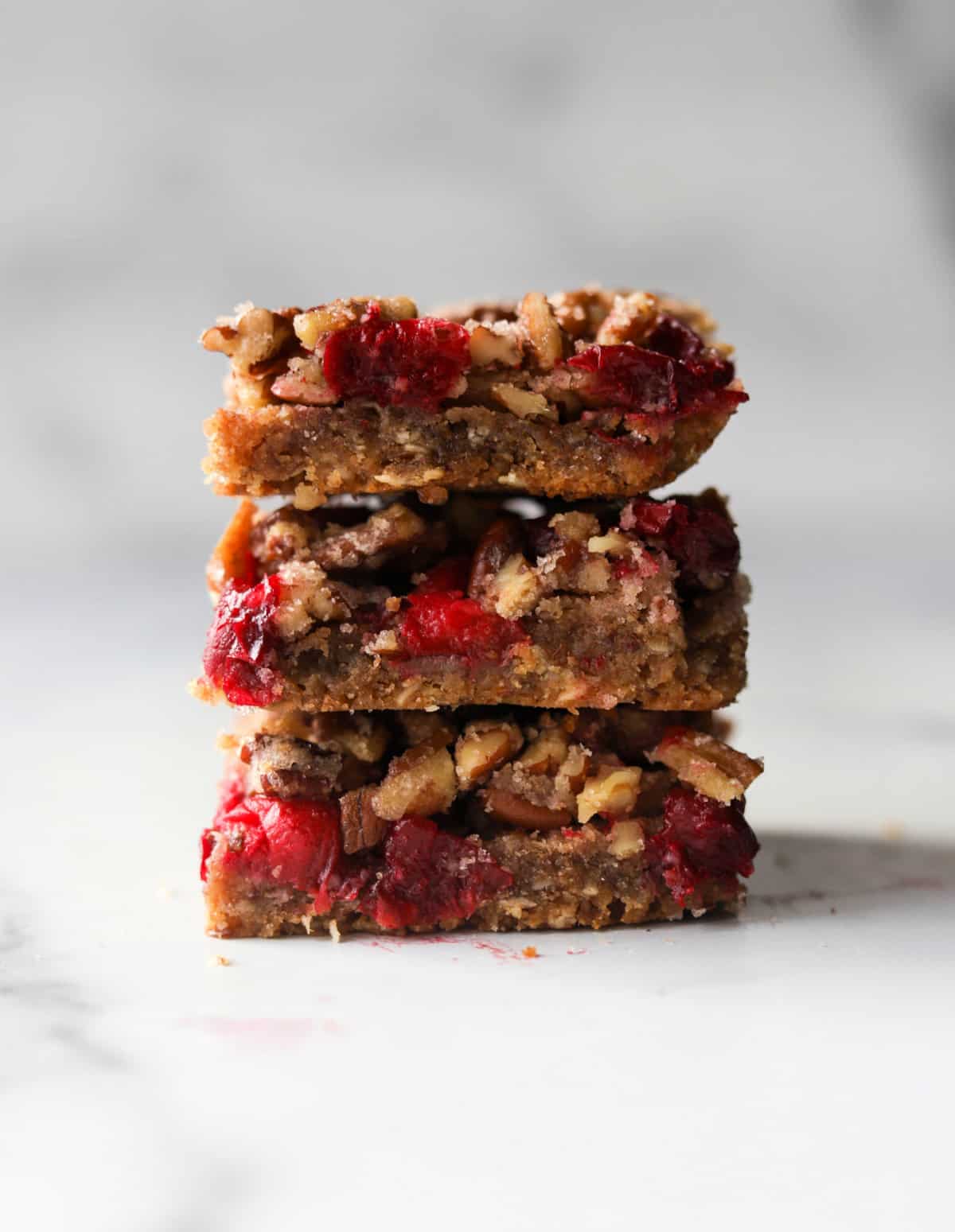 A front shot of a stack of 3 cranberry pecan pie bars.