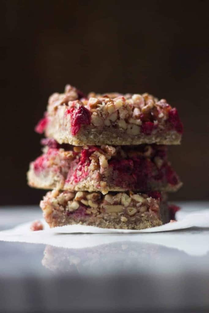Side shot of three cranberry pecan pie bars stacked on top of each other.