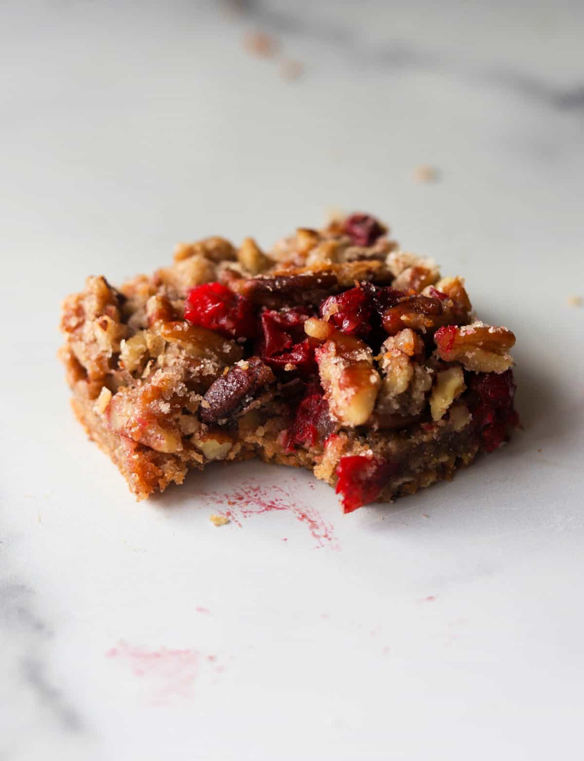 A front shot of a single cranberry pecan pie bar with a bite taken out of it.
