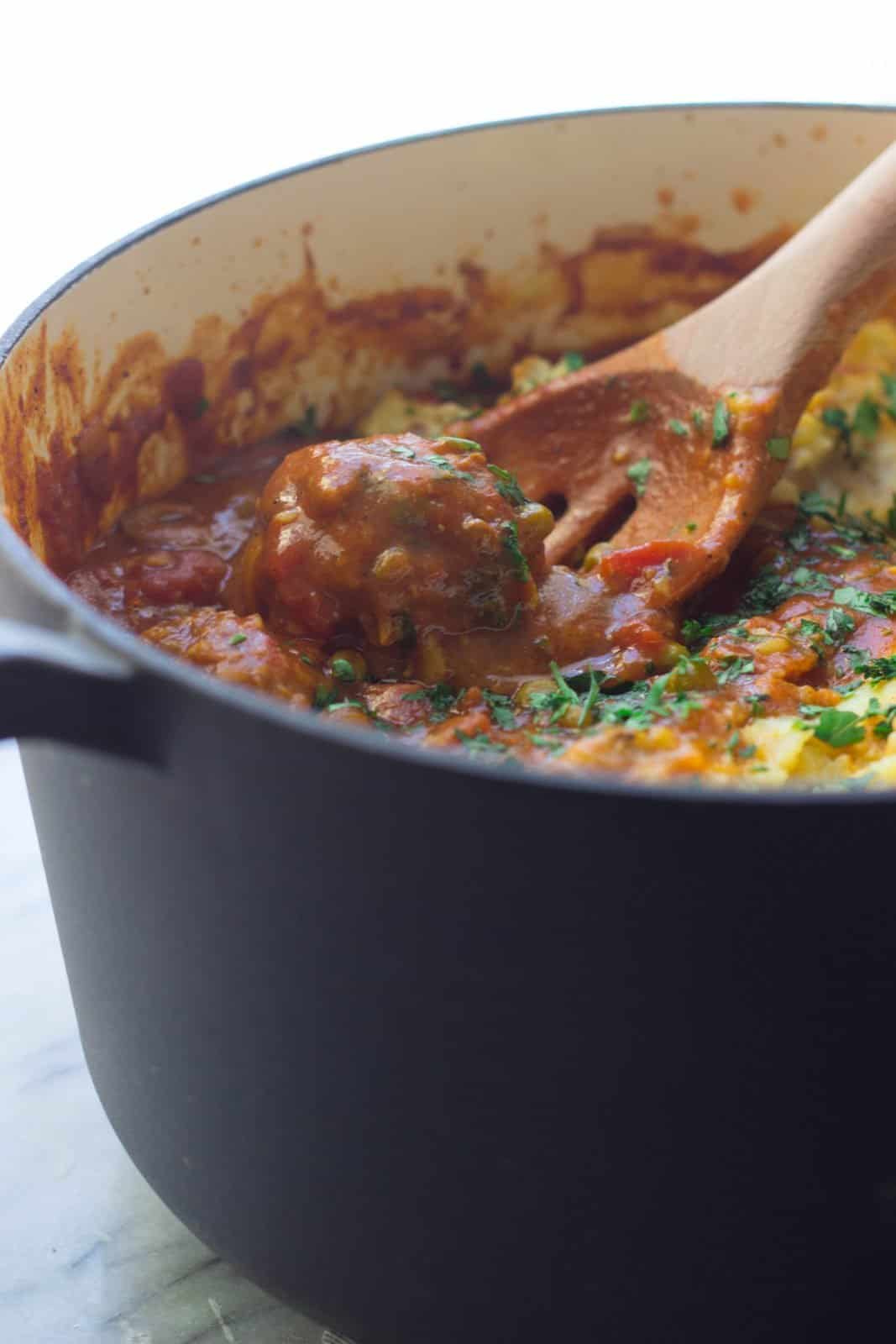Finished recipe of Moroccan-Style Shepherd's Pie with Lamb Lentil Meatballs in a ceramic pot with wooden spoon.