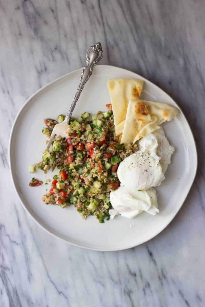 Overhead shot of breakfast tabbouleh with poached eggs and pita wedges on a white plate