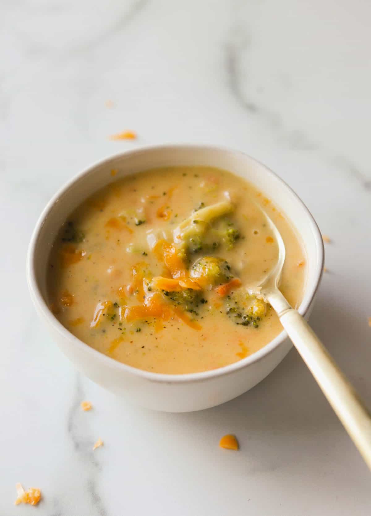 A side shot of a bowl of broccoli cheese soup with a spoon.