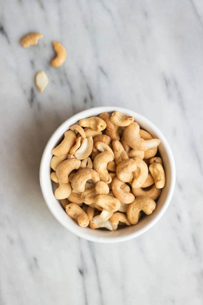 Overhead shot of raw cashews in a white bowl.