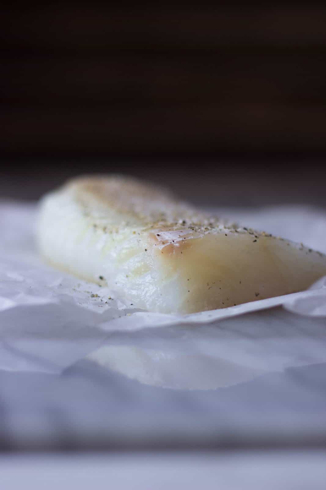 Raw cod with pepper on top of white parchment paper